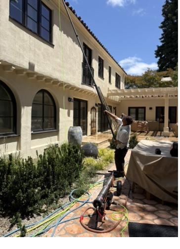 Nick's technician soft washing a two-story stucco home with an extension pole