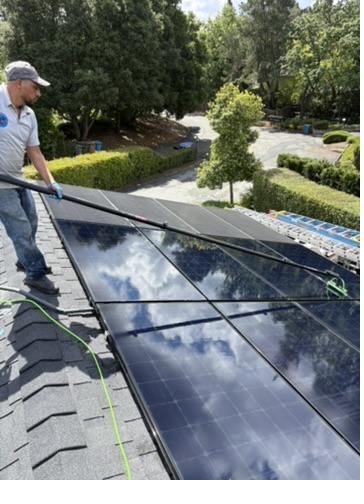 Technician cleaning rooftop solar panels with a soft brush and pure water